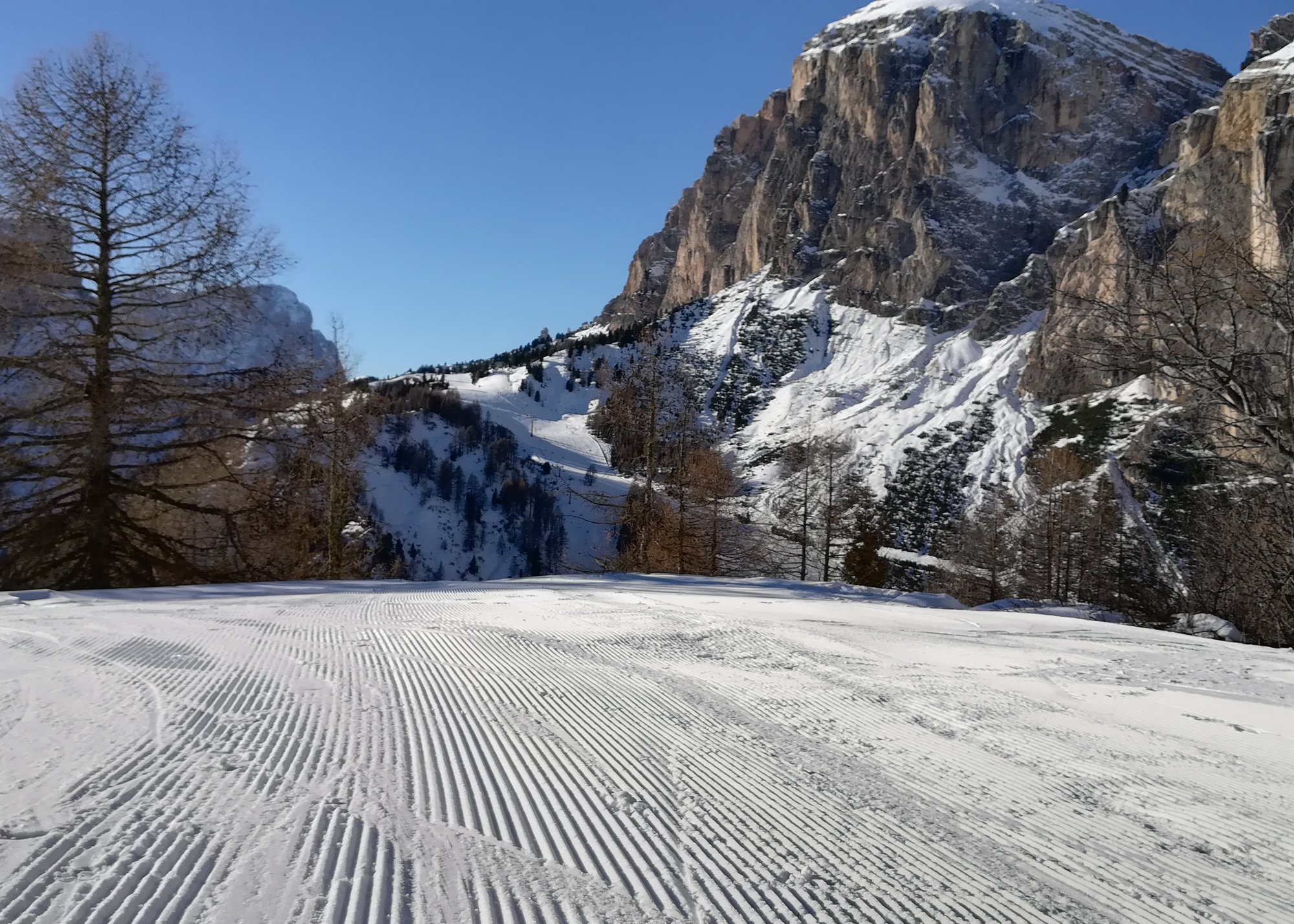 Skiers on a wide groomed run below the limestone walls of the Sella massif